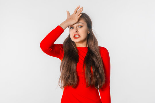 Oops. Lovely young woman makes mistake. Amazed surprised girl in red shirt looks looks awkward and guilty, stands against white studio background