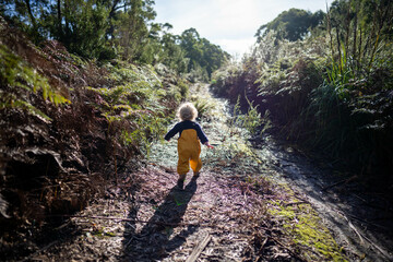 toddler exploring in yellow overalls in the forest