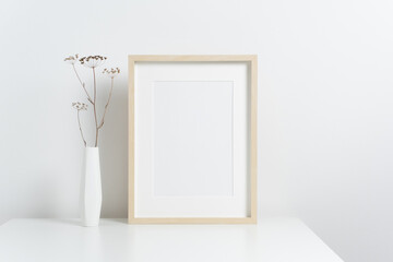 Blank vertical art frame mockup in white interior with stylish botanical decor