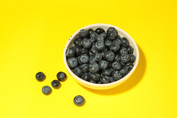 Fresh blueberry in bowl on yellow background. Space for text. Concept of healthy and dieting eating