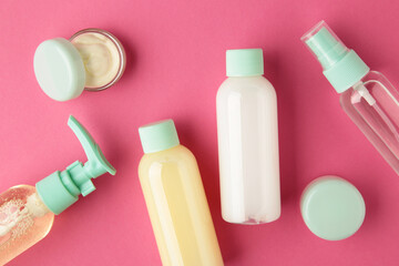 Travel cosmetic bottles on pink background. Minimalist bodycare beauty products for vacation or journey. Top view. Copyspace.