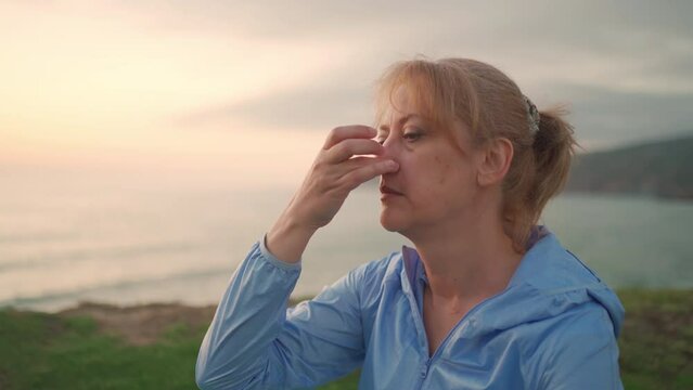 Yogi female doing breathing exercises sitting on ocean shore. Senior woman performing breathing pranayama outdoors ocean background during sunset. Feeling harmony. Healthy senior lifestyle