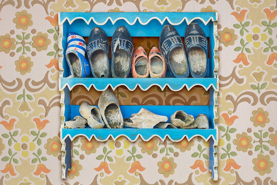 Old cabinet with weathered vintage Dutch wooden clogs on a wall with retro wallpaper