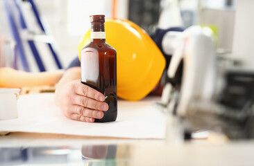 Arm of drunken worker in yellow helmet hold liquor bottle sleeping at table closeup. Manual job workplace DIY inspiration fix shop hard hat industrial education profession career