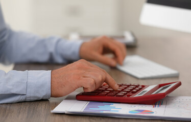 Professional accountant using calculator at wooden desk, closeup