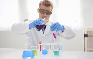 Male chemist holds test tube of glass in his hand overflows liquid solution of potassium...