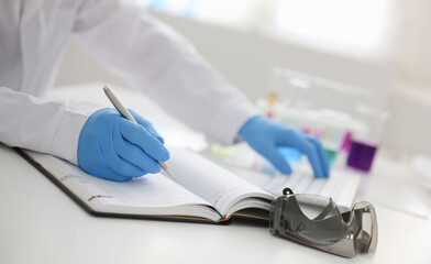Employee of the chemical laboratory teacher chemist holds silvery pen in his hand makes notes in...