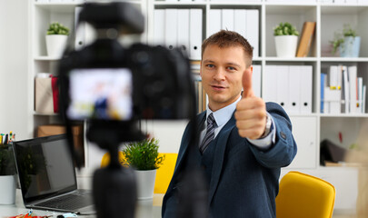 Male in suit and tie show confirm sign arm making promo videoblog or photo session in office camcorder to tripod portrait. Vlogger promotion selfie solution or finance advisor management information © H_Ko