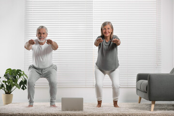 Senior couple practicing yoga with laptop on carpet at home