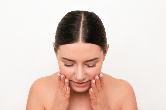 A Young Attractive Caucasian Dark-haired Woman With Beautiful Skin Leaning Forward Washing Her Face With Both Hands Isolated On A Light Background