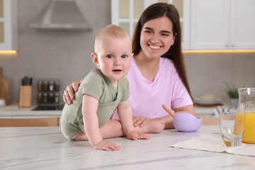 Happy young woman and her cute little baby cooking together in kitchen