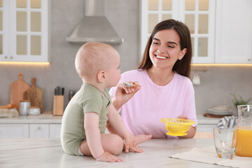 Happy young woman feeding her cute little baby at table in kitchen