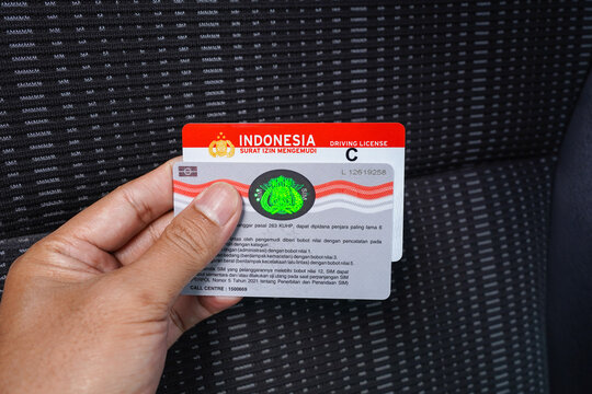 Jakarta, Indonesia - September 18, 2022 : male hand holding a new model SIM A (driving license), sim C, insurance card, and the information on the back of the sim card