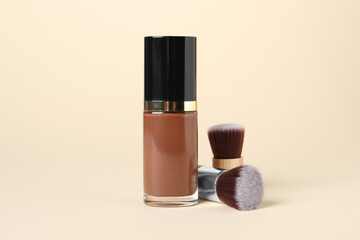 Bottle of skin foundation and brushes on beige background. Makeup product