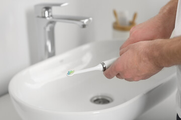 Man holding electric toothbrush near sink in bathroom, closeup