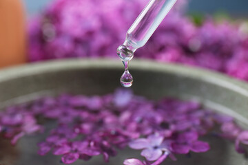 Obraz na płótnie Canvas Dripping essential lilac oil into bowl, closeup