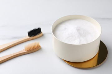 Bamboo toothbrushes and bowl of baking soda on white marble table, closeup