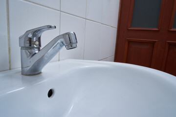 metallic faucet with running water in a white bathroom
