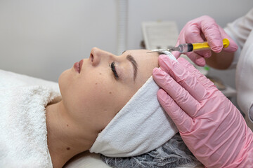 closeup of cosmetologist hand doing treatment procedure with injecting botox in woman client face