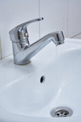 metallic faucet with running water in a white bathroom