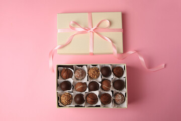 Box of delicious chocolate candies on pink background, flat lay