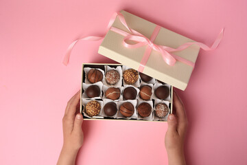 Child with box of delicious chocolate candies on pink background, top view