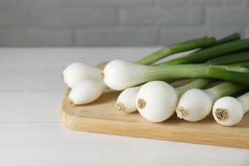 Fresh green spring onions on white wooden table, closeup. Space for text