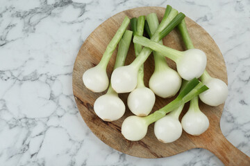 Wooden board with green spring onions on white marble table, top view. Space for text