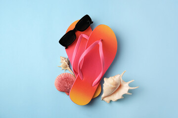 Sunglasses, flip flops and shells on light blue background, flat lay. Beach accessories - obrazy, fototapety, plakaty