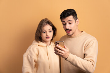 surprised couple checking smartphone  in beige colors. network, messaging, internet concept.