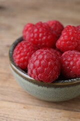 Tasty ripe raspberries in bowl on wooden table, closeup