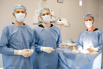Portrait of team of three surgeons ready for surgery in the operating room. Concept of teamwork and...