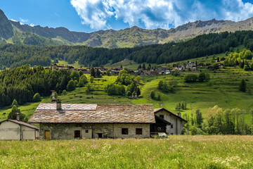 Rural house on the meadow and small village on the mountain slope in Aosta Valley, Italy. - obrazy, fototapety, plakaty
