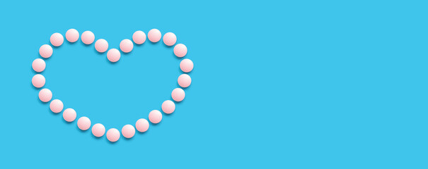 A group of pink round pills form a heart shape on a blue background. The theme of healthcare, treatment and prevention of diseases. World Heart Day