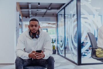 African American businessman wearing headphones while using a smartphone, fully engaged in his work at a modern office, showcasing focus, productivity, and contemporary professionalism