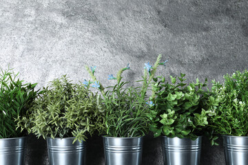 Different artificial potted herbs near grey wall
