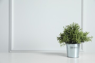 Artificial potted rosemary on wooden table near white wall, space for text