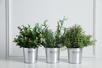 Different artificial potted herbs on wooden table near white wall