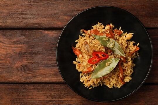 Delicious pilaf and bay leaves in bowl on wooden table, top view. Space for text
