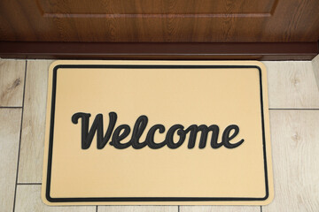 Beautiful beige doormat with word Welcome on floor near entrance, top view