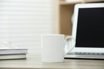 White ceramic mug, notebooks and laptop on wooden table indoors