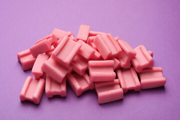 Tasty pink chewing gums on purple background, closeup