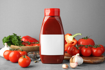 Bottle of tasty ketchup and ingredients on grey table. Space for text
