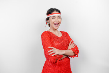 A confident Indonesian woman folding her arms and wearing red kebaya and Indonesia's flag headband to celebrate Indonesia Independence Day. Isolated by white background.