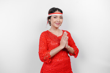 A friendly Indonesian woman is wearing red kebaya gesturing traditional greeting and Indonesia's...