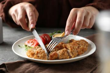 Woman eating delicious schnitzel at grey table, closeup