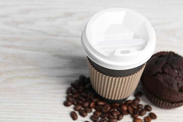 Paper cup, coffee beans and muffin on white wooden table, closeup with space for text. Coffee to go