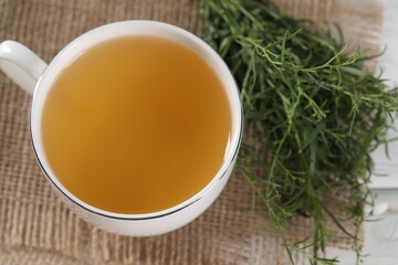 Aromatic herbal tea and fresh tarragon sprigs on table, above view