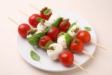 Caprese skewers with tomatoes, mozzarella balls, basil and pesto sauce on beige background, closeup