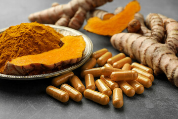 Aromatic turmeric powder, pills and raw roots on grey table, closeup